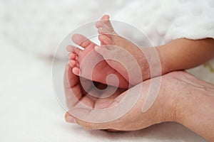 Mother hand holding newborn baby feet on bed