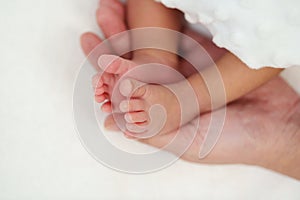 Mother hand holding newborn baby feet on bed