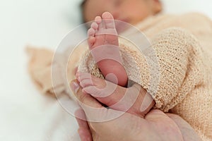 Mother hand holding newborn baby feet on bed