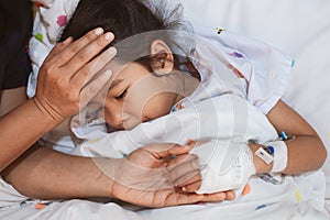 Mother hand holding sick daughter hand who have IV solution bandaged with love and care while she is lying down on bed