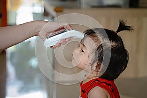 Mother hand measuring temperature baby girl at home . Baby allow mother takeing temperature for toddler with Infrared