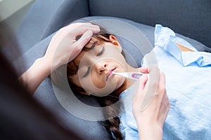 Mother hand taking temperature with girl is a sick laying on sofa, Kid patient with mom check thermometer