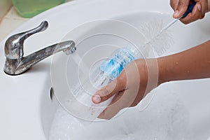 Mother hand washing baby milk bottle on white sink