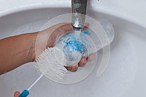 Mother hand washing baby milk bottle on white sink