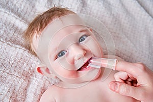 Mother hands brushing teeth with a finger brush of a happy infant baby. Mom doing oral hygiene to a smiling toddler kid, six to