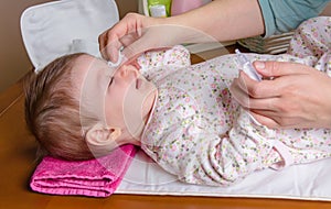 Mother hands cleaning eyes of baby with cotton