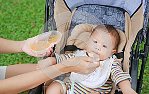 Mother hands feeding food for baby on stroller in green park