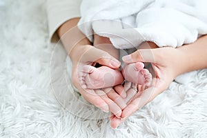 Mother hands hold her newborn baby feet and set shape as heart symbol on white bed