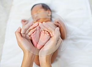 Mother hands hold little newborn baby feet with love emotion and the baby is sleeping on white bed