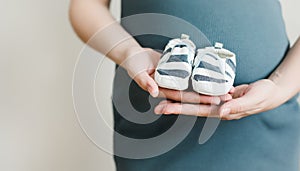 Mother hands holding shoes for the newborn baby. Pregnant woman touching belly. Happy woman pregnancy, maternity, body care