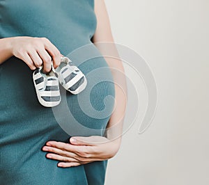 Mother hands holding shoes for the newborn baby. Pregnant woman touching belly. Happy woman pregnancy, maternity, body care