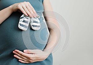 Mother hands holding shoes for the newborn baby. Pregnant woman touching belly. Happy woman pregnancy, maternity, body care