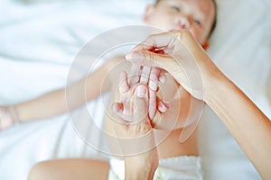 Mother hands massaging finger of baby on the bed at home