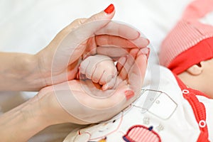 Mother hands with red nails holding newborn arm.