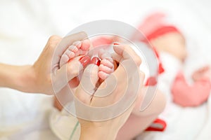 Mother hands with red nails holding newborn baby legs.