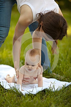 Mother and happy baby doing exercise routine on green grass outdoors