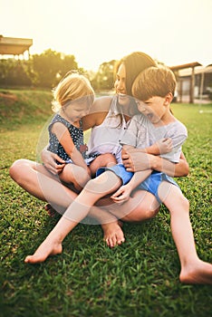 Mother, happy children or hug playing on grass for fun bonding in summer outside a house in nature. Funny mom hugging