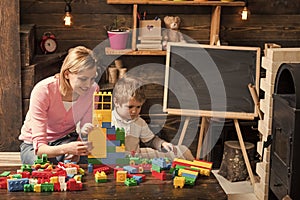 Mother and happy son play with constructor. Motherhood concept. Nursery with toys and chalkboard on background, copy
