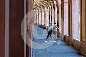 Mother with hat and daughter with hand on her hip standing in portico i