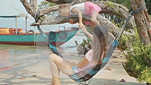 Mother having fun with her little cute daughter on hammock at the sandy beach