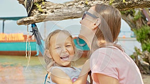 Mother having fun with her little cute daughter on hammock at the sandy beach