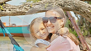 Mother having fun with her little cute daughter on hammock at the sandy beach