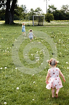 Mother having quality funny playing time with her baby girls at a park blowing dandelion - Young blonde hippie -