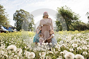 Mother having quality funny playing time with her baby girls at a park blowing dandelion - Young blonde hippie -