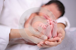 The mother held the baby in her hand. Mom holding small baby feet. Woman hands holding newborn baby feet