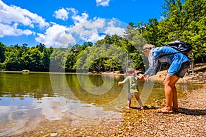 Mother help baby enter feet in lake water during family trip in nature of Foresta Umbra - Gargano Apulia - Italy photo