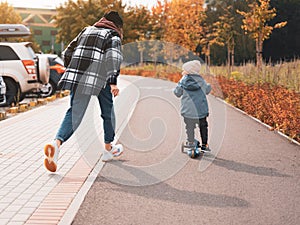 Mother help her son ride with kick scooter. Happy family mother teaches child son to ride a scooter in the Park. Support