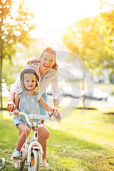 Mother helping baby girl riding bicycle in park