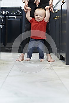 Mother Helping Baby Son To Walk In Kitchen