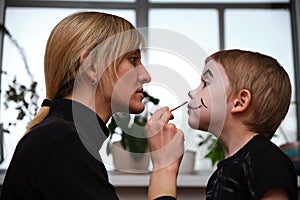 Mother is helping caucasuan son with Halloween makeup indoor