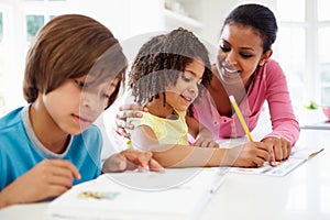 Mother Helping Children With Homework In Kitchen