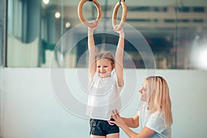 Mother helping daughter to play sports on gymnastic rings