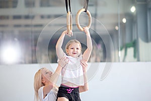 Mother helping daughter to play sports on gymnastic rings