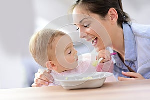 Mother helping her baby girl eating