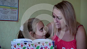 Mother helping her daughter do homework. Girl makes lessons, reading, writing