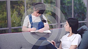 Mother is helping her daughter doing homework while relaxing in living room on a sofa.