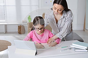 Mother helping her daughter doing homework with tablet at home