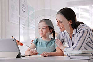 Mother helping her daughter doing homework with tablet at home