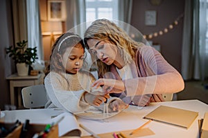 Mother helping her daughter with homework, drawing a circle with comasses in evening at home.