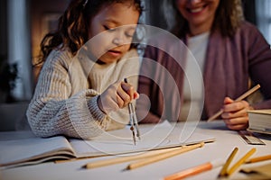 Mother helping her daughter with homework, drawing a circle with comasses in evening at home.