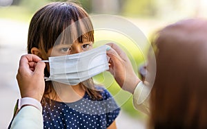 Mother helping her daughter to wear medical face mask