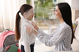 Mother helping her little daughter to get ready for school indoors