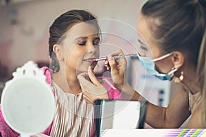 Mother helping her little girl with make up