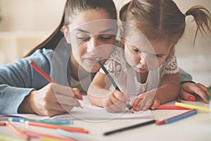 Mother helping her little girl to writing at home.