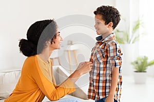 Mother helping her son button up shirt in living room