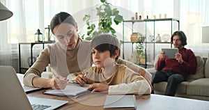 Mother helping son doing homework using laptop and father using digital tablet